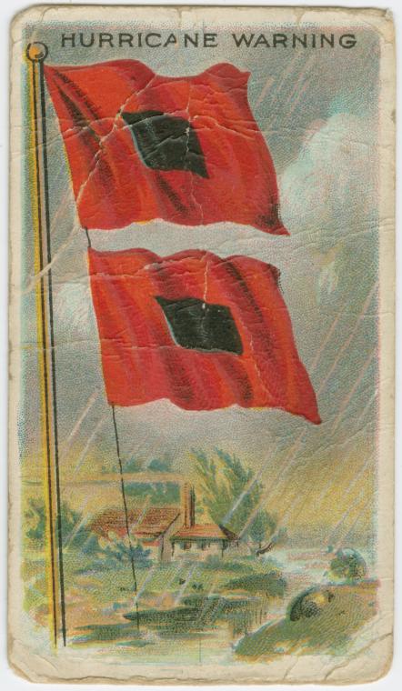 Universally recognized Hurricane Warning flags. Two red flags with black squares in the center and a beachfront home in the background.