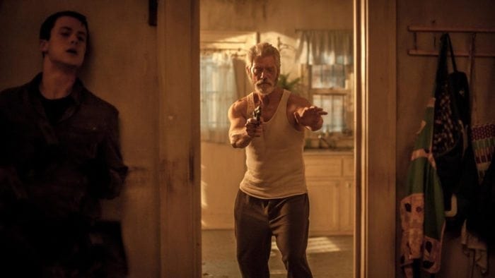 "The Blind Man" played by Stephen Lang walking through a doorway holding a handgun.