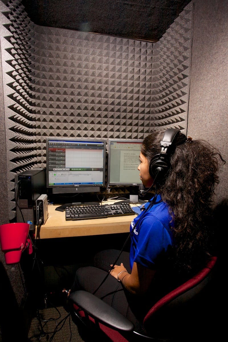 A Braille Works employee reading and recording an audio document in a recording booth.