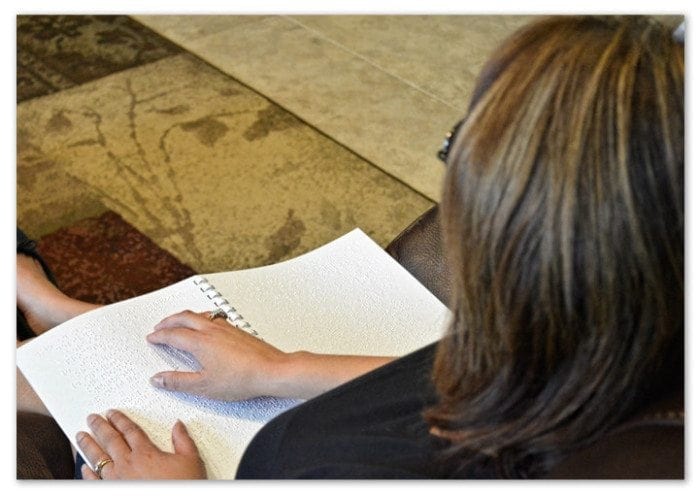 Woman sitting in her living room reading a braille utility statement.