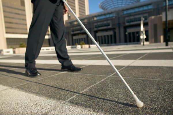Image showing a business person walking down a sidewalk with a white cane while the sunshine casts shadows.