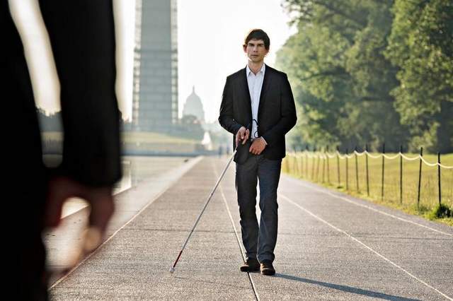 Auggie Anderson walking down waterfront sidewalk with his white-cane during an episode of Covert Affairs