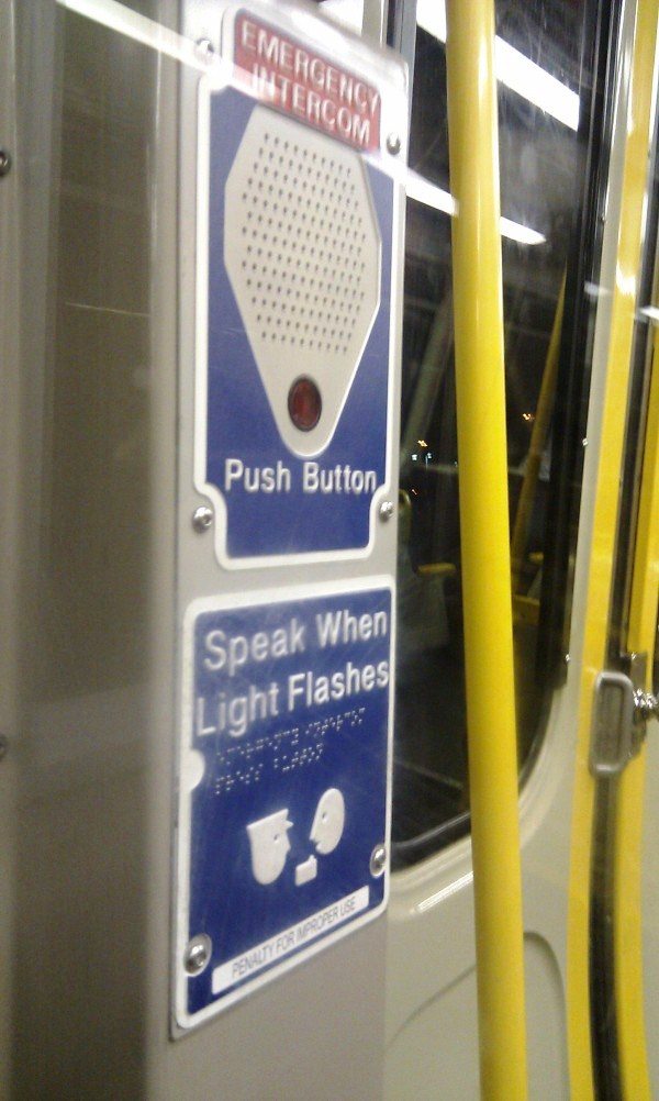 Subway emergency intercom with the phrase "speak when the light flashes" written in print and braille.