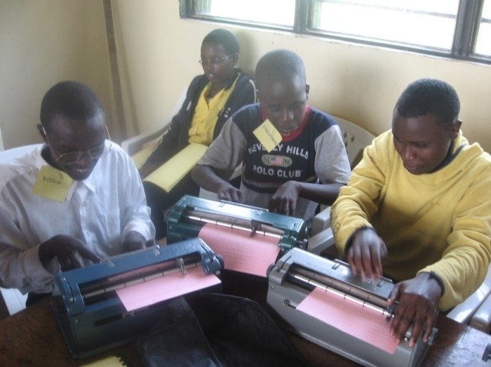 Image showing several students working with Perkins Braillers to create braille documents at the HVP Gatagara School for the Visually Impaired.