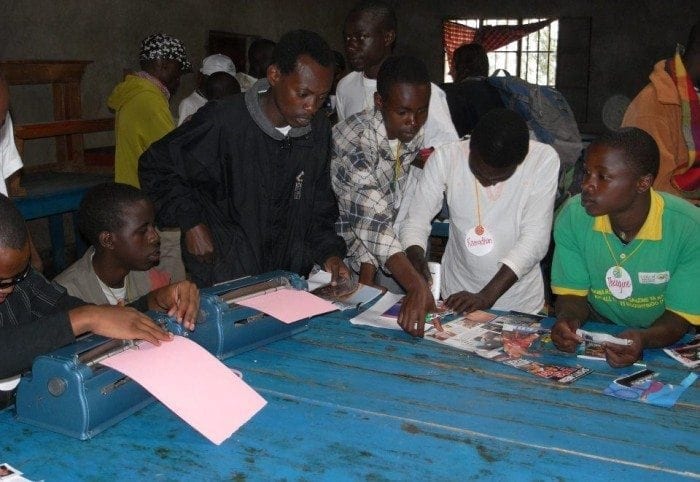 Image showing Eric Niyikiza working on an art project with several boys at Camp BE. 