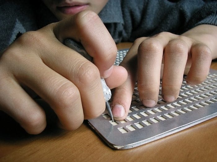 Close-up view of a child with visual disability using a slate and stylus tool to write braille