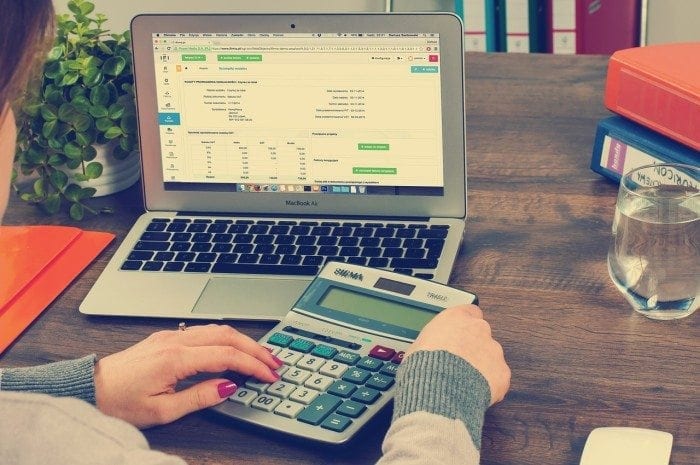 Person's hands holding a calculator in front of a laptop