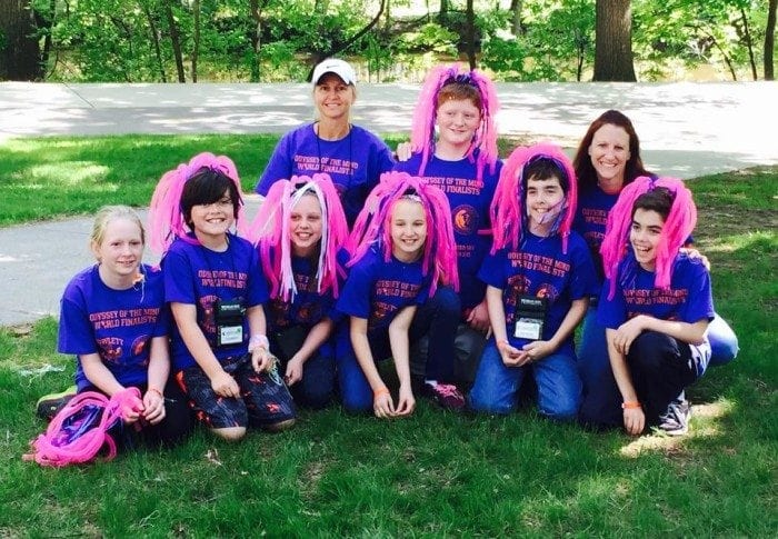 The odyssey of the mind team of seven children and two adults, holding and wearing cheerleader pom poms on their heads while sitting on the ground. The odyssey of the mind team of seven children and two adults, holding and wearing cheerleader pom poms on their heads while sitting on the ground.