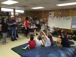 Lou and Joyce Fioritto speaking in a classroom in front of students, who are seated on the floor in front of them. Lou and Joyce Fioritto speaking in a classroom in front of students, who are seated on the floor in front of them.