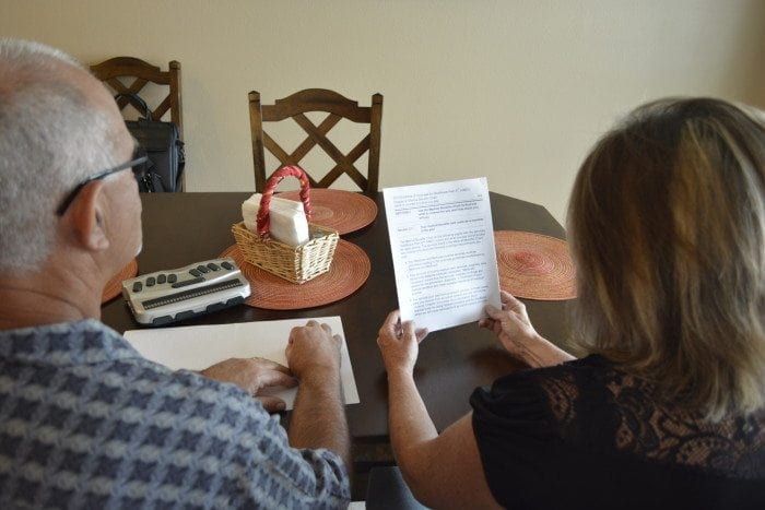 Image showing an over-the-shoulder view of a man and woman sitting the their kitchen table reading Braille and Large Print documents.