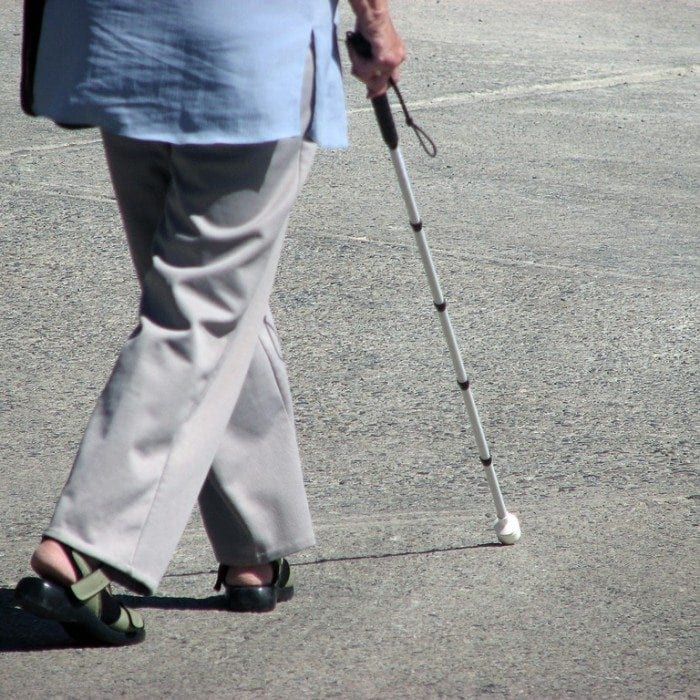 Image showing a woman in business clothing walking down a sidewalk with a white cane in-hand.