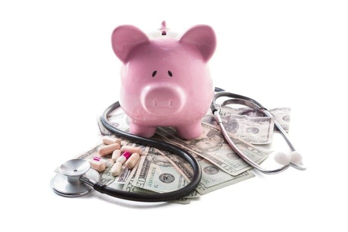 Piggy bank, medication and stethoscope resting on pile of dollars