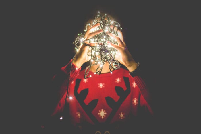 Person wearing a Christmas sweater holding a balled up string of Christmas lights
