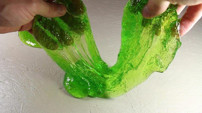 Child's hands holding and stretching green slime.