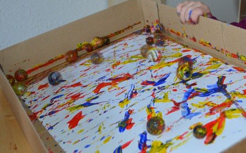 Paint covered marbles rolling around on paper, leaving paint on the paper as they roll.