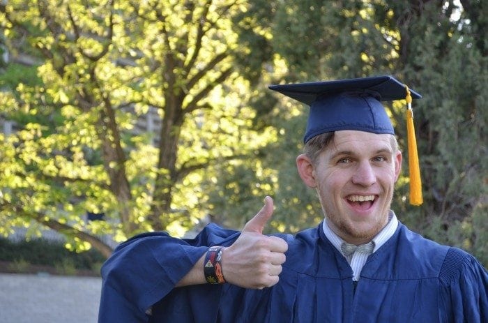 A young man wearing a graduation cap and gown, smiling and giving a thumbs up.