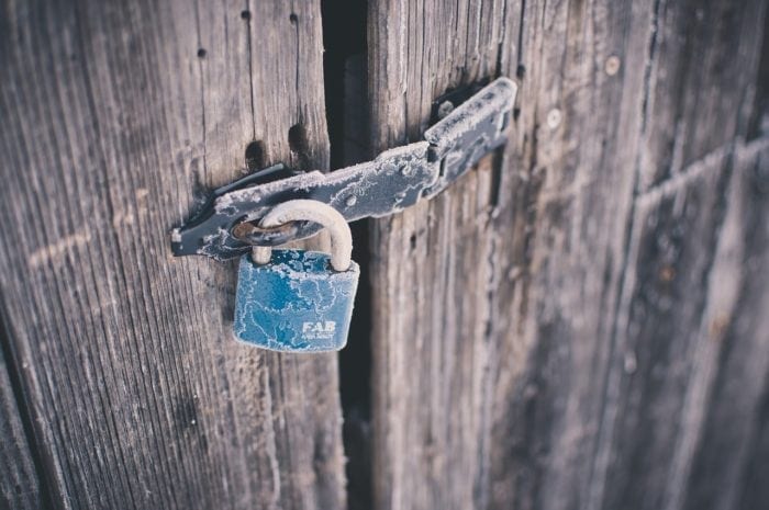 Padlock on wooden door that's frozen over with frost that prevents accessibility to the other side
