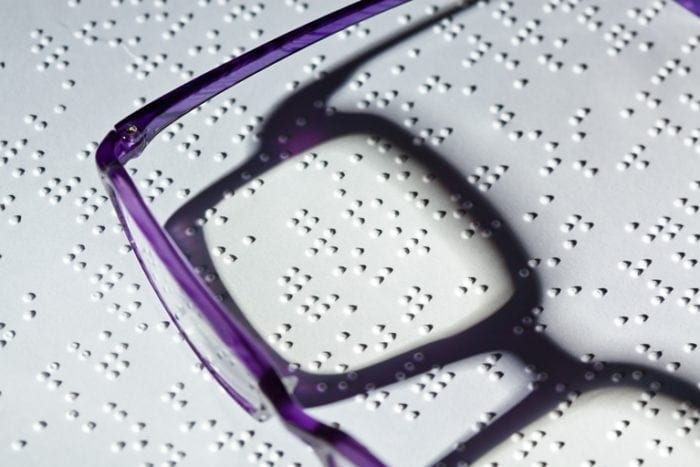 Purple glasses resting on top of a braille document.