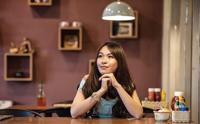 Woman sitting at a table. Her chin is resting on her hands while she thinks.