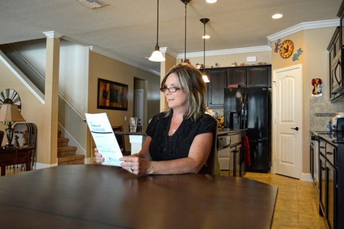 Woman sitting at her kitchen table reading a large print document.