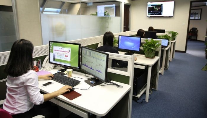 Four women sitting at their desks working on computers and laptops.