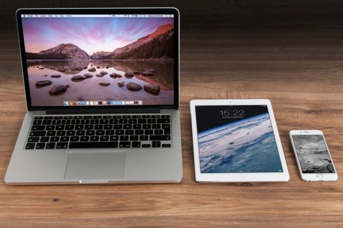 Apple Macbook, iPad and iPhone resting on a wooden tabletop.