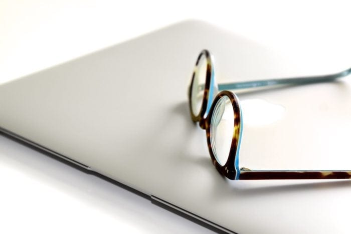 A pair of glasses resting on top of an Apple Macbook.