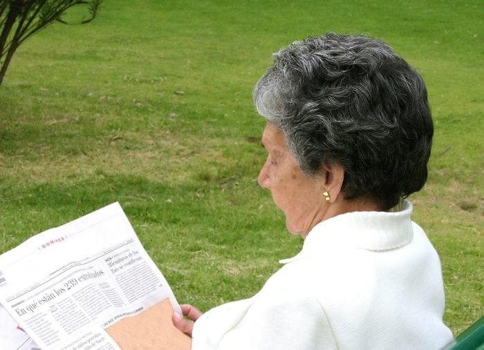elderly woman reading her form of communication-- a newspaper