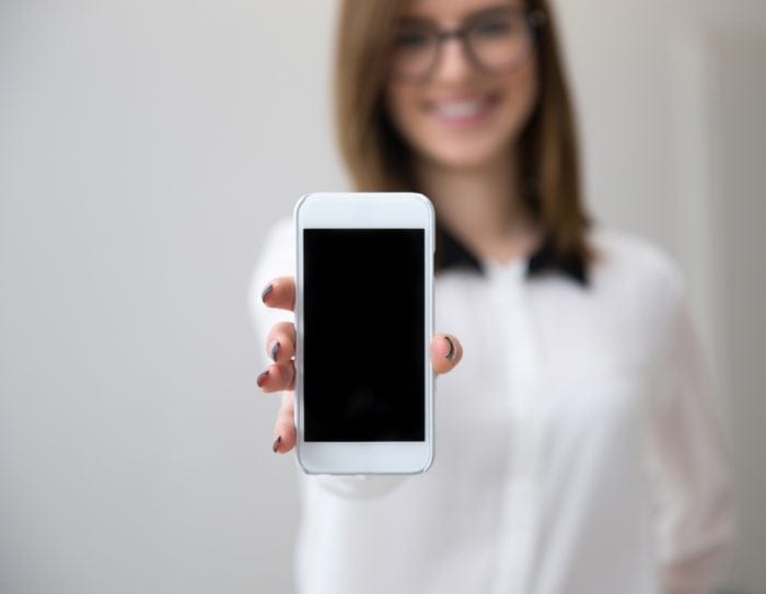 Businesswoman holding a smartphone with a blank screen. The focus is on the smartphone, and the rest of the image is blurred.