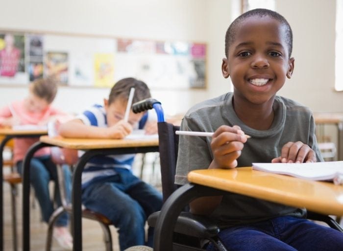 african american boy in a wheelchair with a smile on his face and the classroom aisles are clear