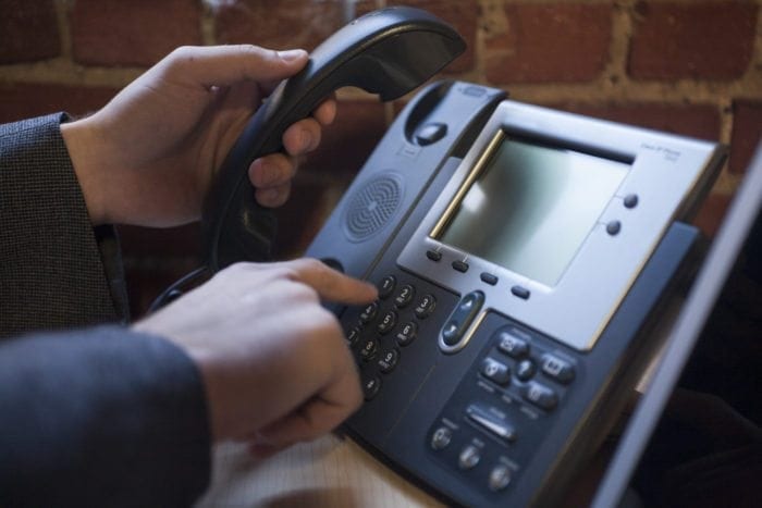 Hands picking up a phone receiver and dialing a phone number
