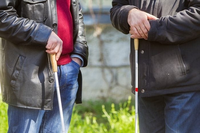 The torso's of 2 people standing outside, each holding a white cane