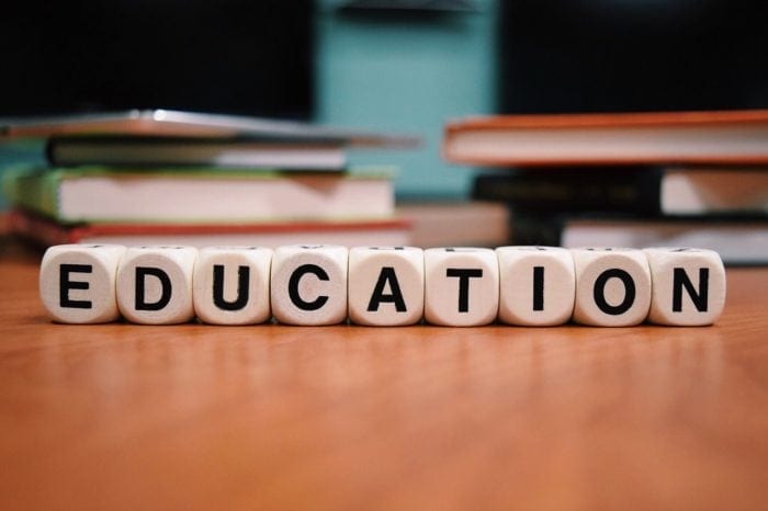 Letter cubes that spell "education" on a desk with books in the background