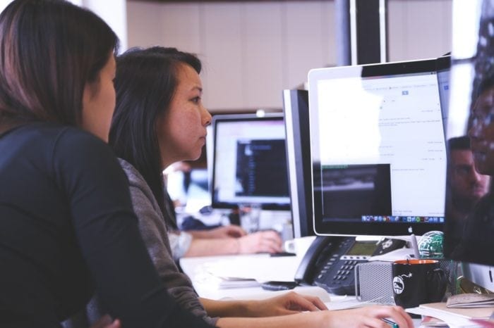 Two people sitting at a desk looking at a screen