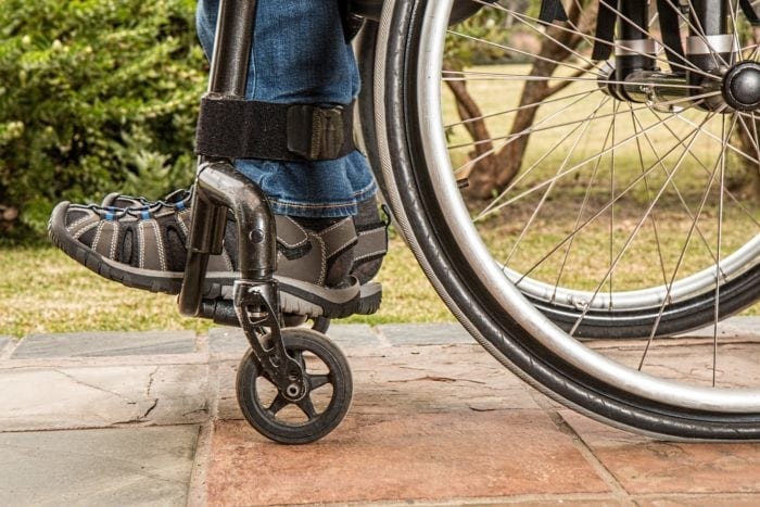 Tennis shows and lower portion of jeans of a person sitting outside in wheelchair