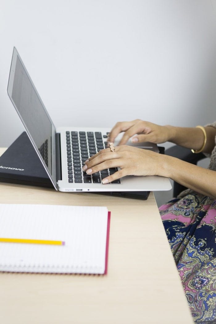 employee typing at a table with a laptop and a notebook nearby