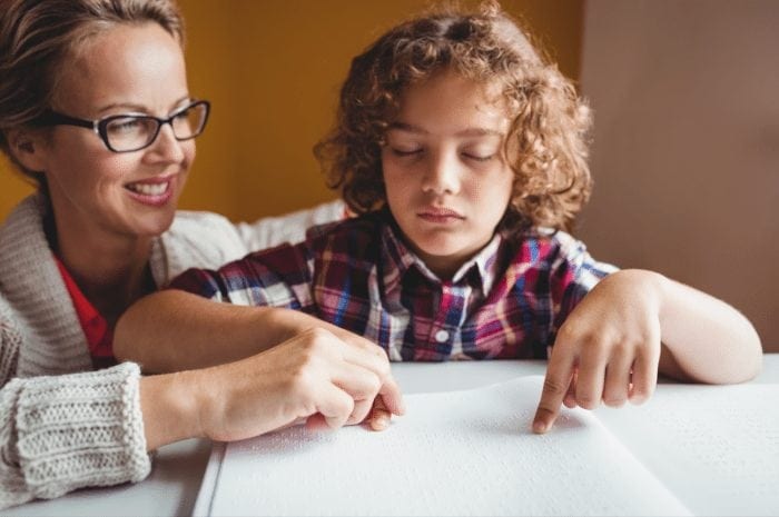 VI Teacher helps a boy learn to braille.