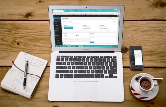 Laptop surrounded by a notebook, cell phone and coffee