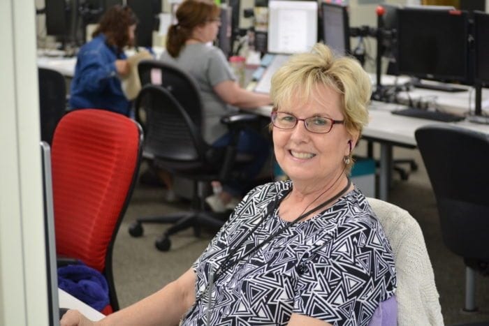 an employee smiling at the camera and working at a computer