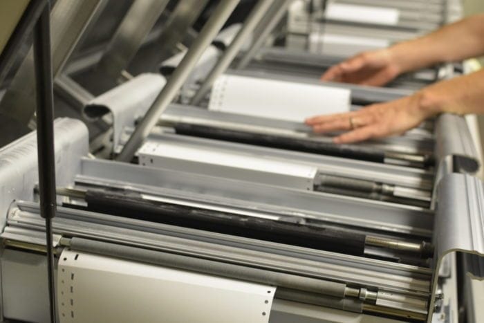 the hand of a braille works employee guiding braille paper across embossers