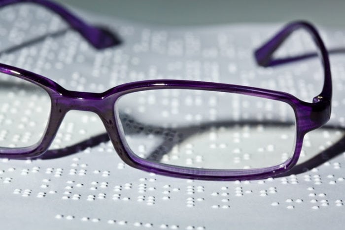 Close-up of embossed braille and a pair of glasses sitting on top