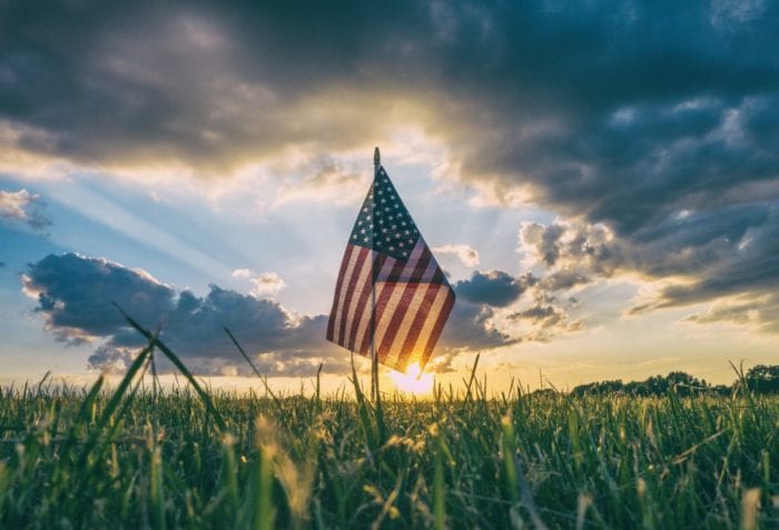 American flag in a field of grass in front of a sunrise.