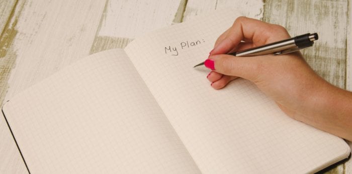Hand holding a pen over a notebook that says, "My Plan:"