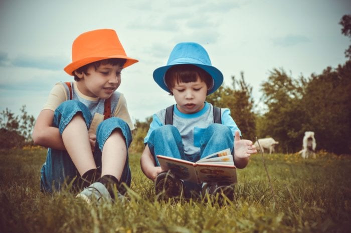 Two young boys sitting in a field with one reading to the other