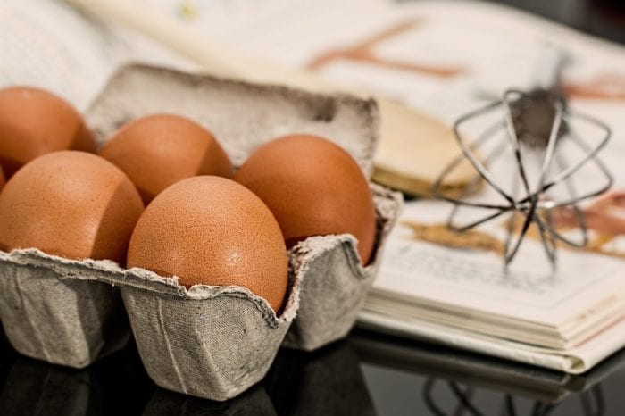 a carton of eggs, a recipe book, and a whisk on the counter