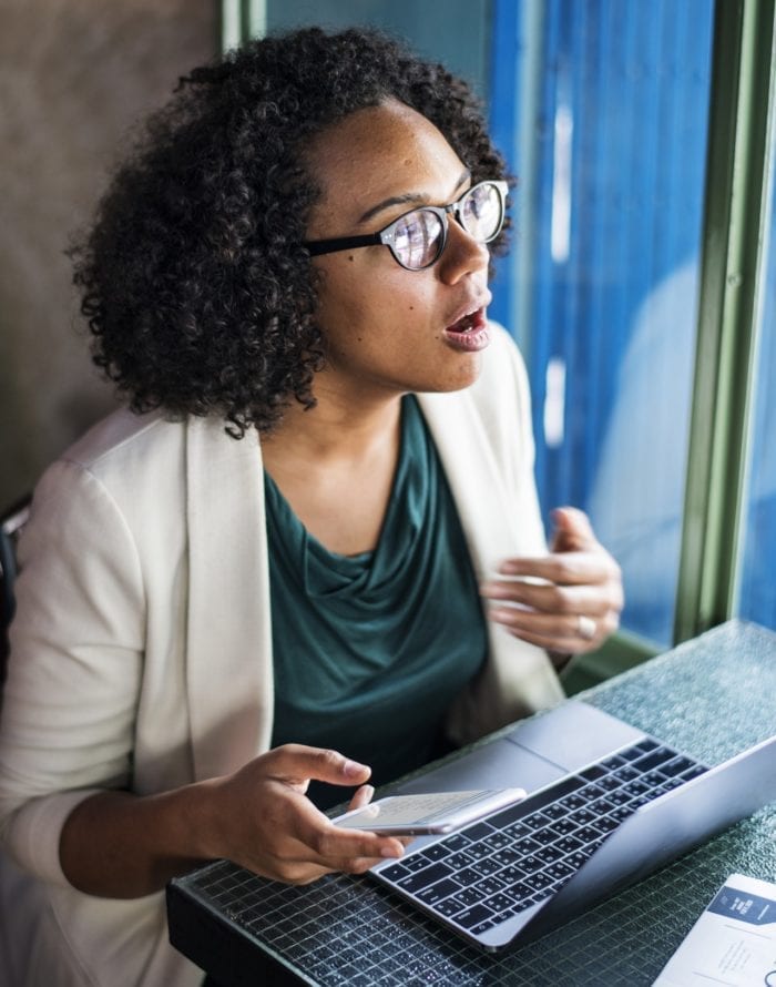 African American businesswoman holding her phone and having her mouth wide open in shock.