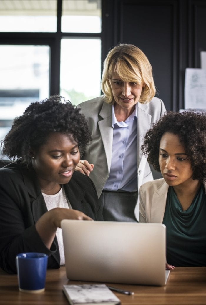 a group of businesswomen standing around a laptop and exchanging ideas