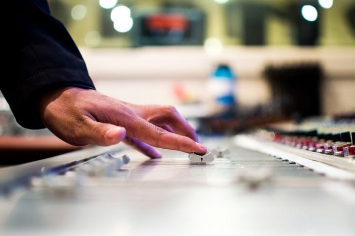 a hand turning the volume on a recording studio mixing desk