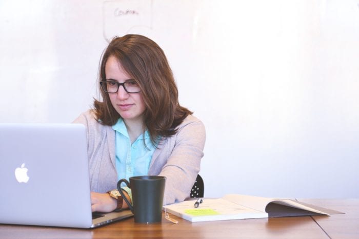 woman sits at her desk with a laptop, notebook, and coffee ready to do research on legal matters