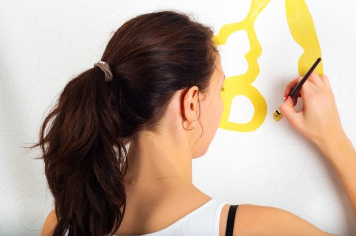 a woman with her back towards a wall painting a DIY with a small paintbrush